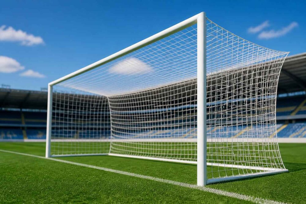 Biała bramka piłkarska z siatką ustawiona na zielonej murawie stadionu przy błękitnym niebie